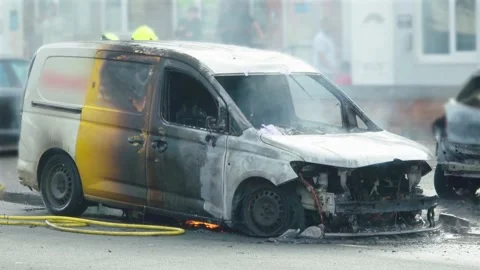 Vehicle fire aftermath with burned van, smoke and small flames beneath chassis Stock Footage 344104191