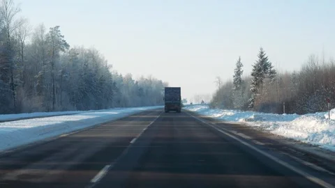 Vehicle navigating icy highway surrounded by frost covered trees under clear sky Stock Footage 327484830