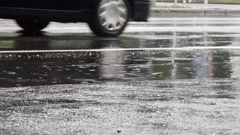 Vehicle tire driving through large puddle on asphalt road, creating splashes of Stock Footage 344862936