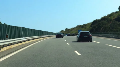 Vehicles drive on a multi-lane road through a hilly landscape on a sunny day. Stock Footage 284300898