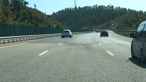  Vehicles drive on a multi-lane road through a hilly landscape on a sunny day. Stock Footage 284350662