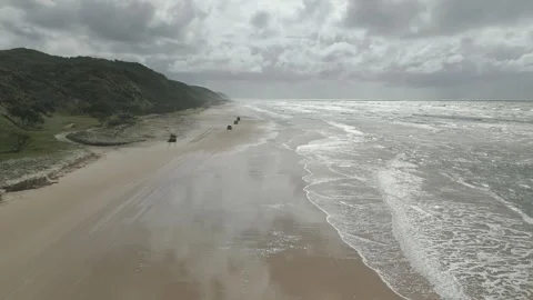 Vehicles driving on wide sandy beach with green cliffs Stock Footage 341617695
