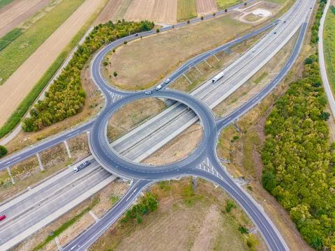 Vehicles move around a roundabout that connects multiple highways. Fields and Stock Photos