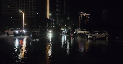 Vehicles navigate a flooded, reflective city intersection during rain at night Stock Footage 336070786