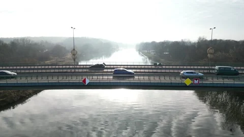 Vehicles traversing a bridge over a reflective river showcasing continuous Stock Footage 324524059
