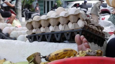 A vendor adjusts egg cartons while customers browse food items in the background Stock Footage 313485928