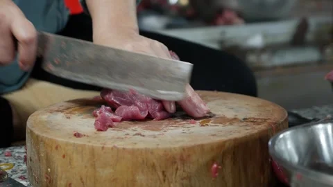 Vendor carefully slices thin pork pieces with a large knife on a wooden chopping Stock Footage 331011741