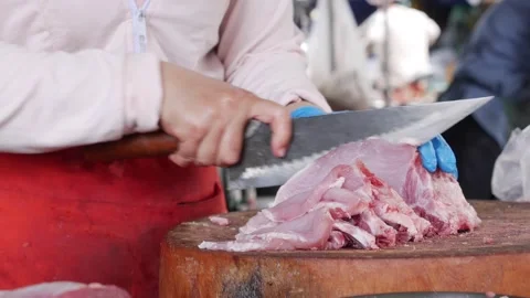 Vendor chops a chunk of pork using a heavy knife on a wooden chopping block Stock Footage 331445750