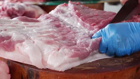 Vendor cuts a large pork piece into smaller portions using a heavy knife on a 库存影片 333632703