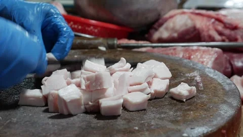 Vendor cuts small cubes of pork fat or lard on a round wooden chopping surface Stock Footage 332300842