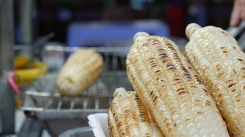 A vendor flips charred corn cobs on a wire grill, ensuring a perfect balance of 스톡 동영상 312108944