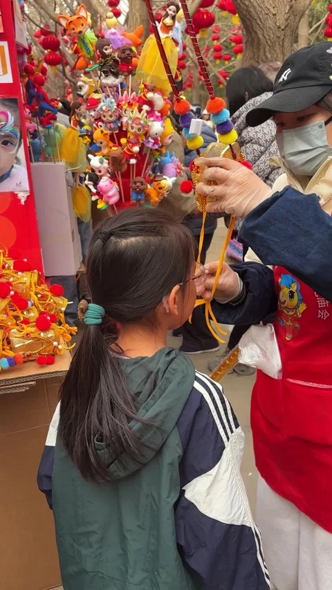 Vendor helping child try on Monkey King hat at Ditan Temple Fair Stock Footage 329847015