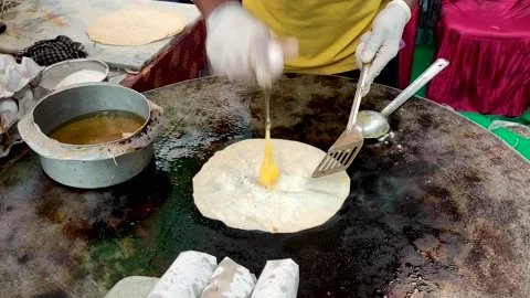 A vendor is preparing a delicious egg roll at a street food stall. Stock Footage 312111322