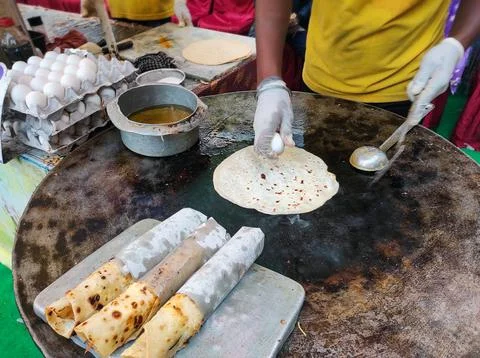A vendor is preparing a delicious egg roll at a street food stall. Stock Photos