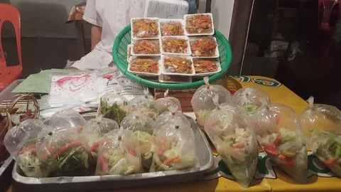 Vendor sells assorted packaged vegetable dishes at night market, Laos Vídeos de archivo 75237298