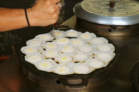 Vendor using tool cutting the edges of nearly done Thai coconut milk pancak.. Stock Photos