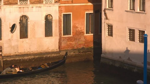 A Venetian gondolier steers a gondola into a small waterway between buildings in Vídeos de archivo 128317841