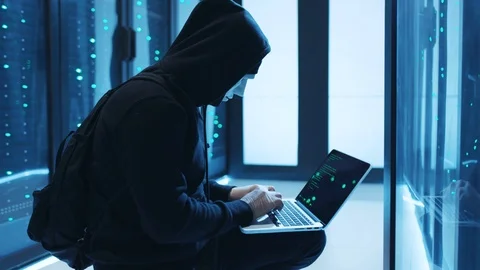 Vengeful hacker in mask programming code on laptop connected to server cabinet Stock Footage 120604341