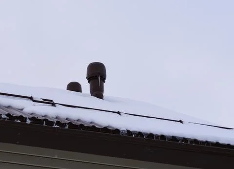 Vent stack with icicles on a snow-covered roof against sky background. Close- Foto stock