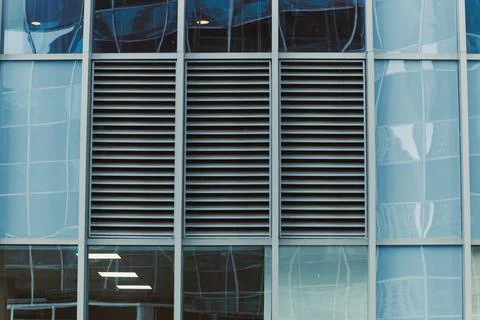 Ventilation grills are set within a building facade featuring large glass win 写真素材