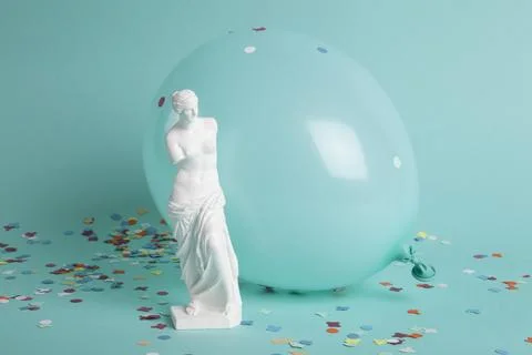 A venus in front of a balloon of the same color as the background and confett Stock Photos