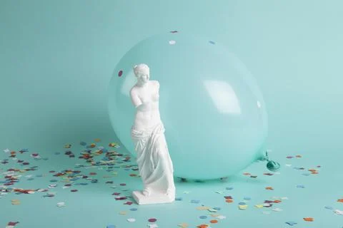 A venus in front of a balloon of the same color as the background and confett Stock Photos