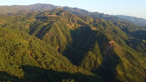 Verdant mountain range covered in lush green trees under a clear blue sky on a Stock Footage 316924895