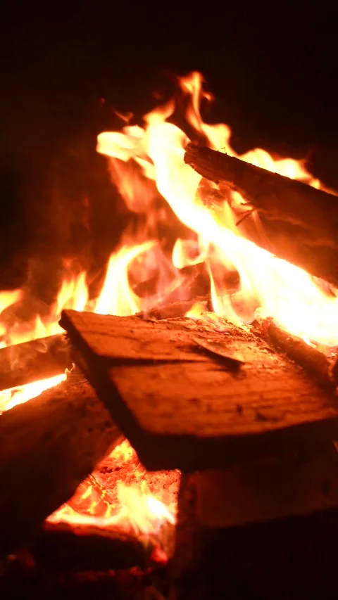 Vertical 4K close-up of mesmerizing campfire flames and sparks at night. Видео 328759203