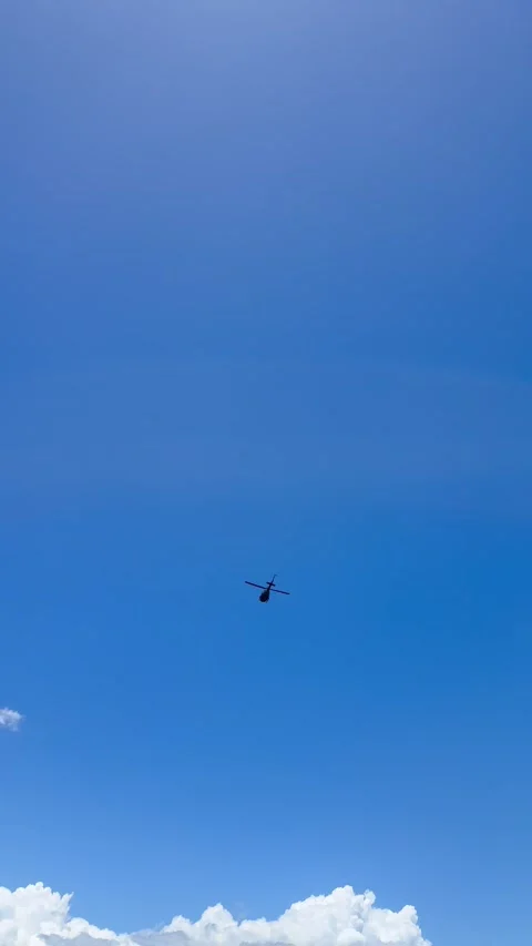 Vertical 4K Distant Helicopter Flying In Clear Blue Tropical Sky Over Ocean Stock Footage 335479530