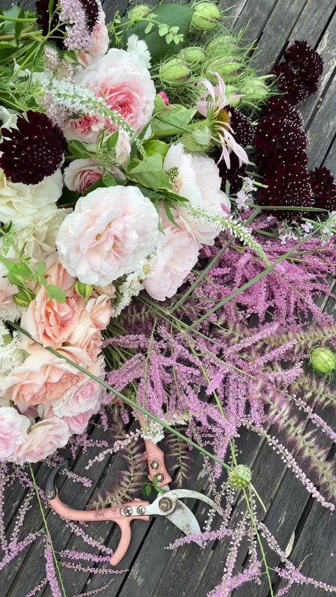Vertical 4K handheld shot of summer bouquet with pink pruners on wooden table. 스톡 동영상 337908319