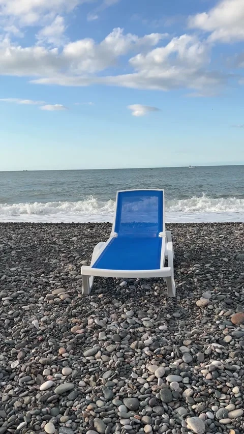 Vertical 4K video. Blue and white sun lounger on shore line of pebble beach Stock Footage 277467219