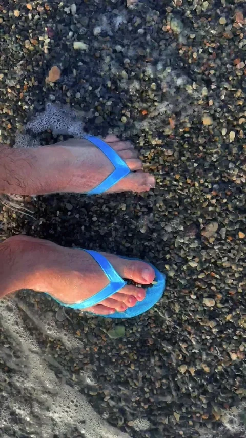 Vertical 4K video. Top view. Male feet in blue shales on shore of pebble beach Stock Footage 277467193