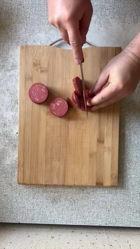 Vertical 4K video. Top view. Man cuts smoked sausage for sandwich with knife Stock Footage 277472164