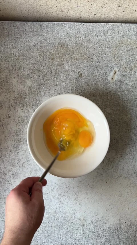 Vertical 4K video. Top view. Man beats egg yolks with fork in white bowl Stock Footage 277616682