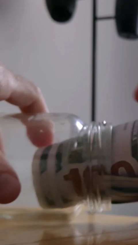 Vertical 4K View of a Man Saving Money by Placing Dollar Bills into a Jar Video stock 285345525