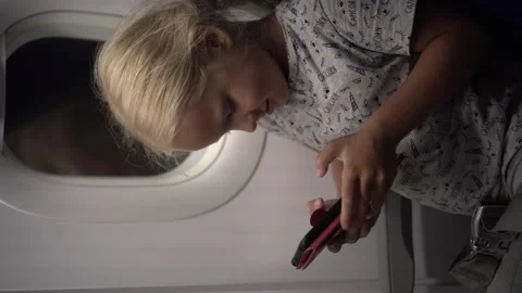 Vertical: A 7-year-old girl uses a smartphone on a plane. Stock Footage 330404700