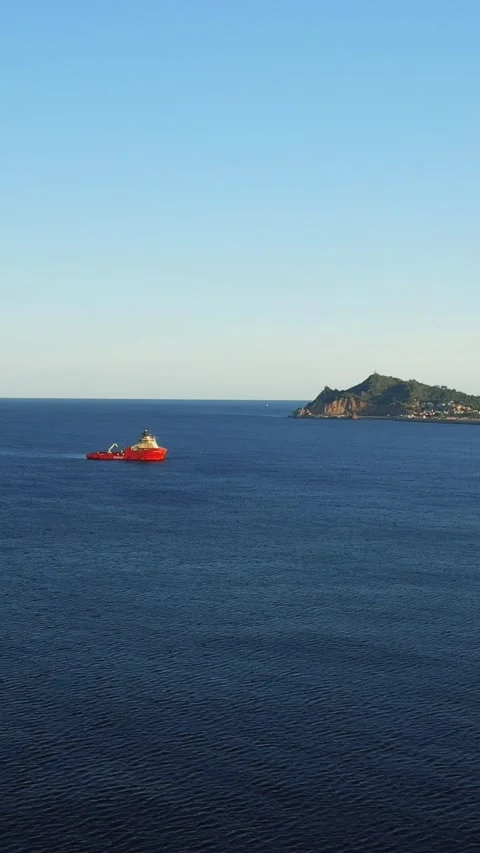 Vertical 9:16 video showing a red boat moving across the calm blue sea in front Stock Footage 346663278