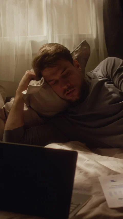 Vertical of Adult Man Lying on Bed Distracted from Online Work by Phone Stock Footage 330610073