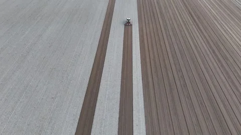 Vertical aerial image shows a tractor smoothing plowed soil across parallel 스톡 동영상 321323345