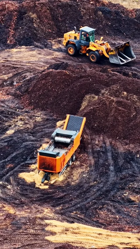 Vertical aerial parallax over wheel loader and wood chipper processing bark Stock Footage 336264853