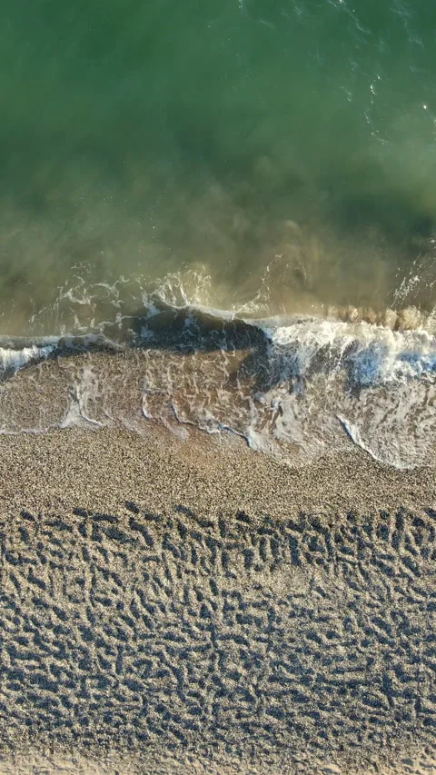 Vertical aerial top down view of sea waves rolling on sandy pebble beach. 스톡 동영상 347737936