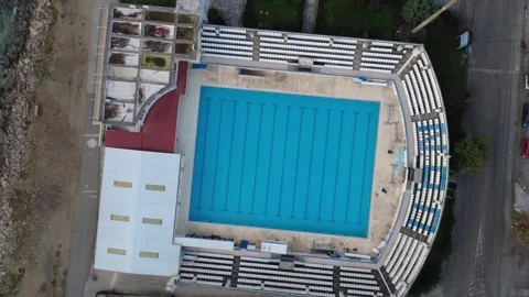 Vertical aerial view empty outdoor swimming pool beside coastal beach Stock Footage 343993814