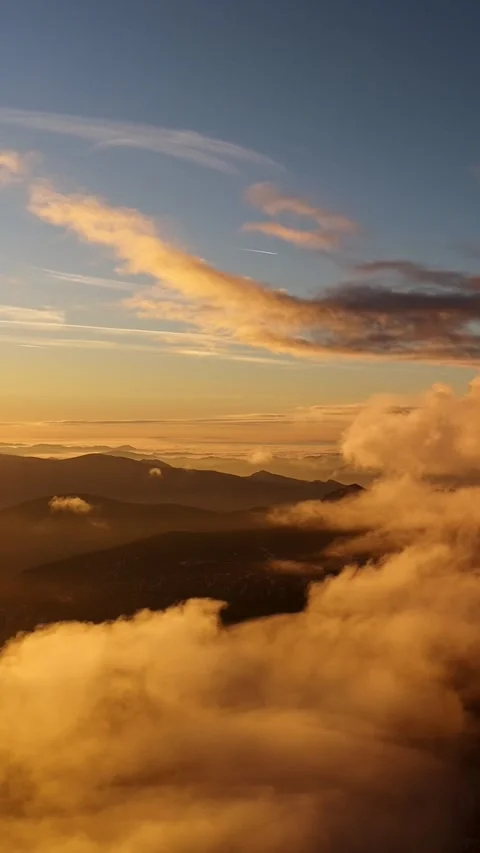 Vertical aerial view of golden clouds and mist over dark mountain ridges during 스톡 동영상 327594590