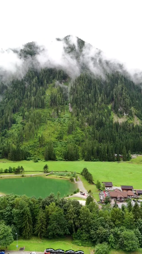 Vertical aerial view of a misty mountain with meadow and calm lake Stock Footage 322045397