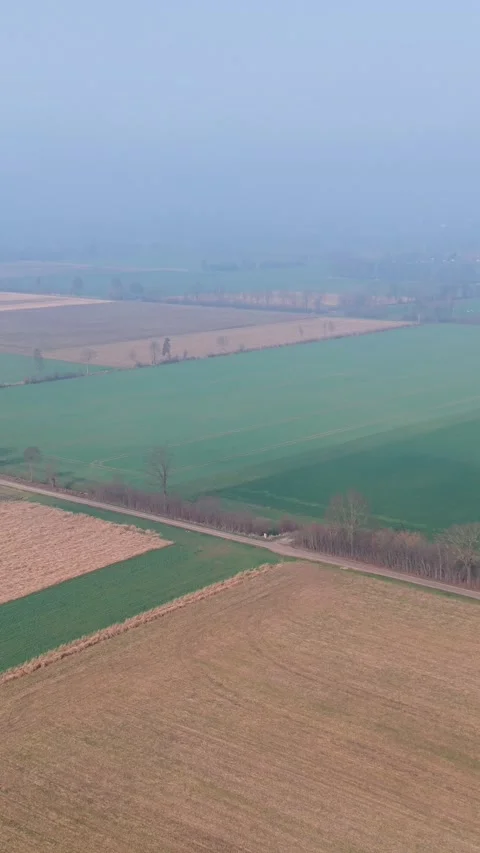 Vertical aerial view of patchwork agricultural fields in a misty rural land Video stock 332741920