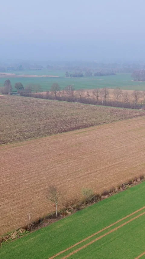Vertical aerial view of patchwork agricultural fields in a misty rural landscape Stock Footage 334628241