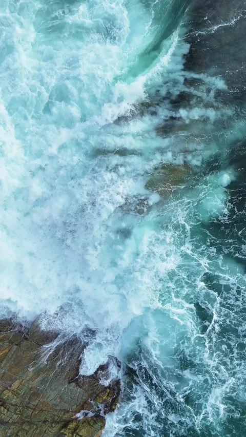 Vertical Aerial View of Powerful Ocean Waves Crashing on Coastal Rocks Video stock 325936731
