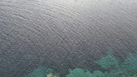 Vertical aerial view of a rugged volcanic island meeting the turquoise sea. Stock Footage 327672294