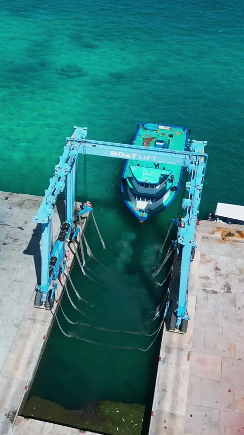 Vertical aerial view of shipyard boat lift crane near vessel in tropical lagoon Stock Footage 346270791