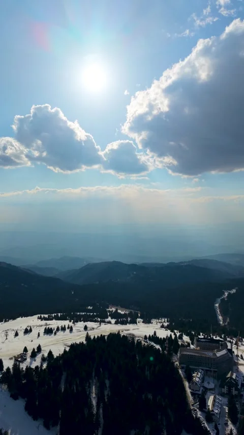Vertical aerial view of ski resort with sun rays piercing through clouds over Stock Footage 332395606